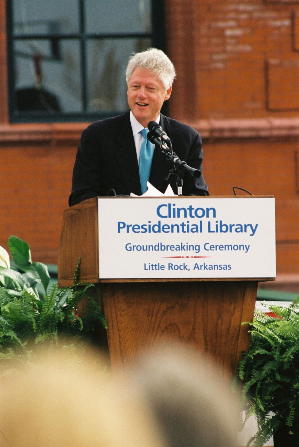 President Clinton speaks behind a podium that says "Clinton Presidential Library Groundbreaking Ceremony"