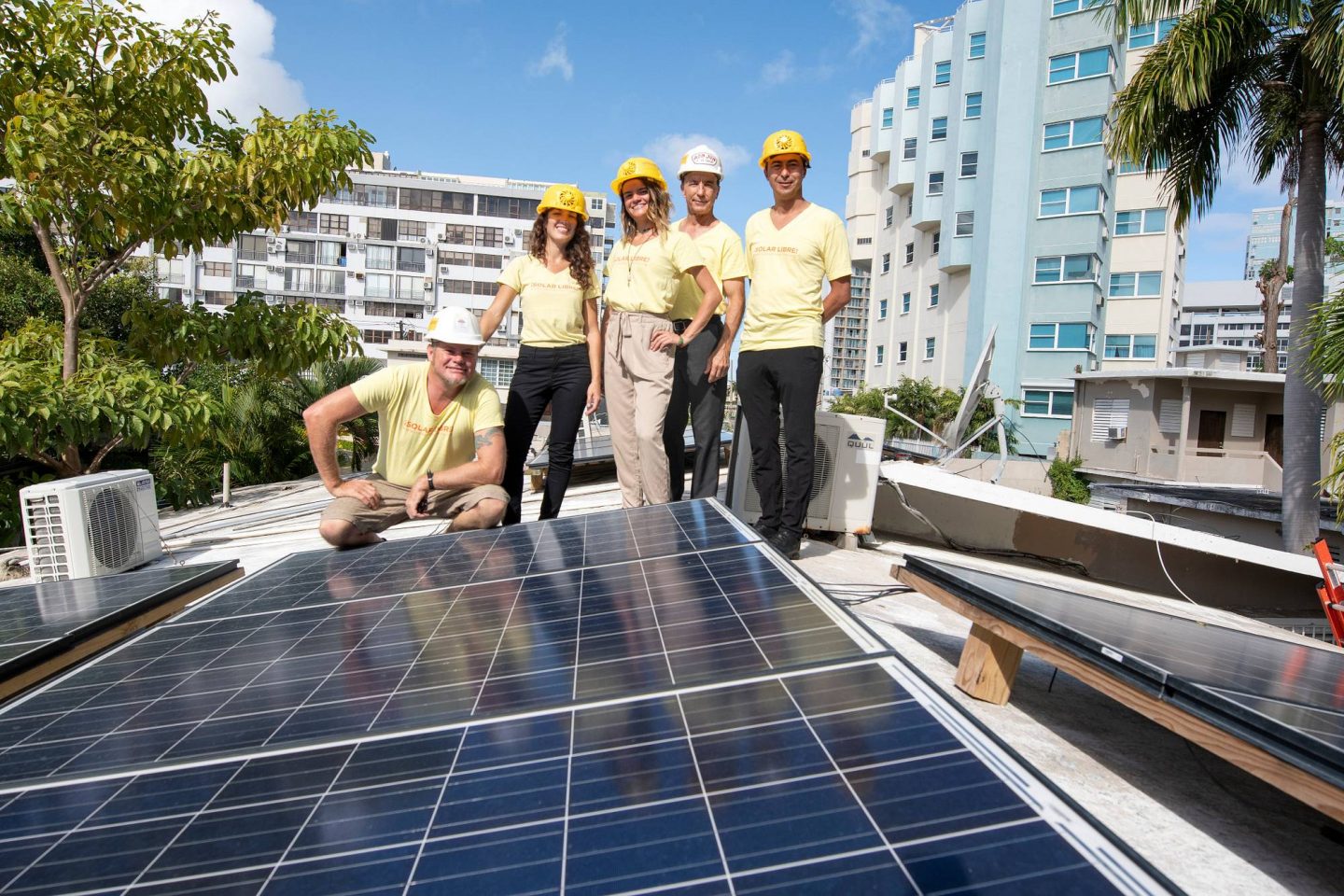 A group of individuals wearing hard hats gather in front of a solar panel