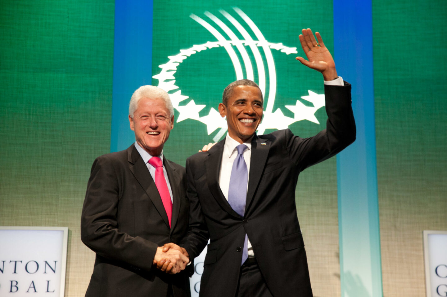 Presidents Bill Clinton and Barack Obama shake hands on stage