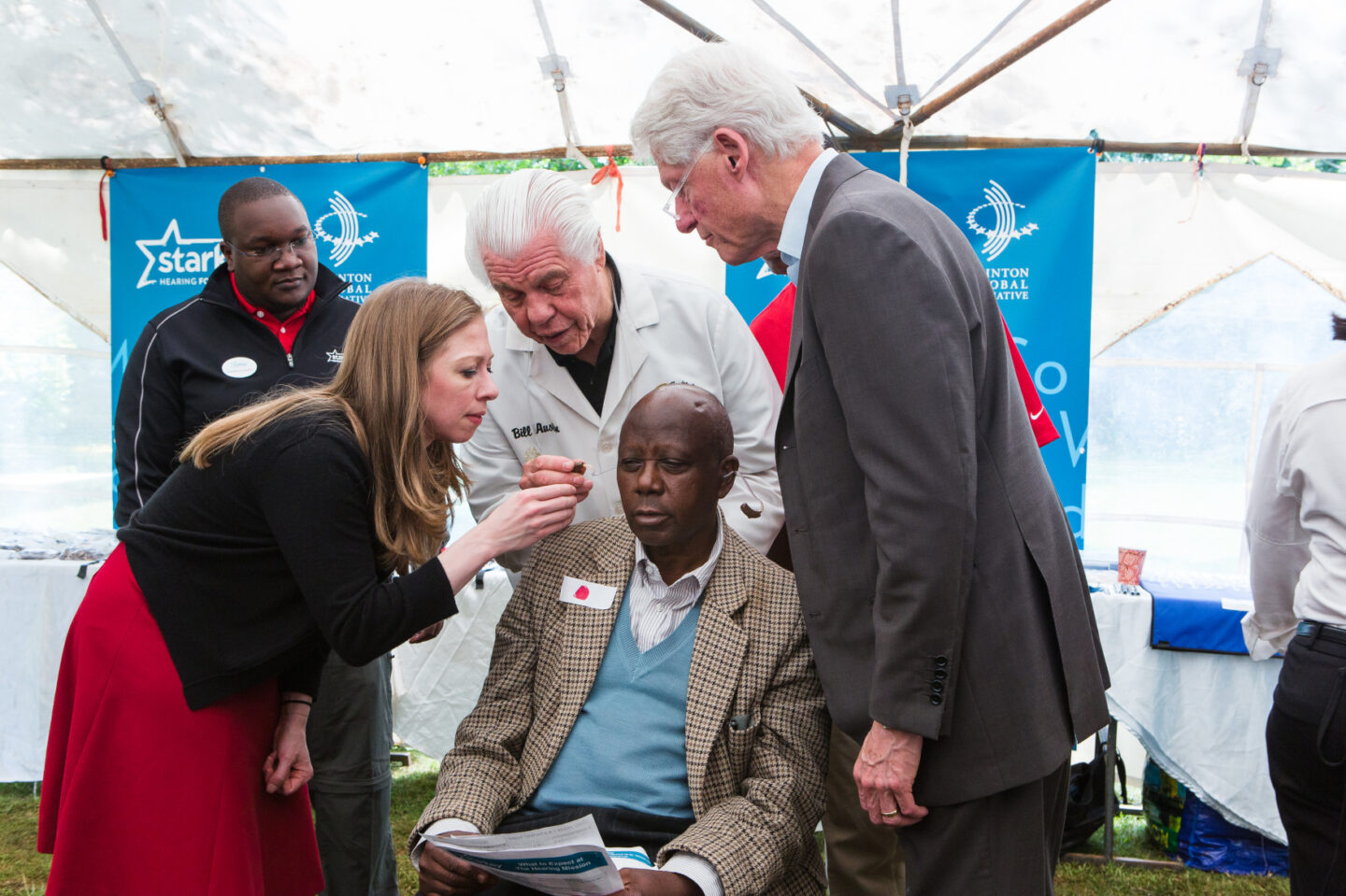 President Clinton and Chelsea Clinton help fit a hearing aid to a man in Nairobi, Kenya