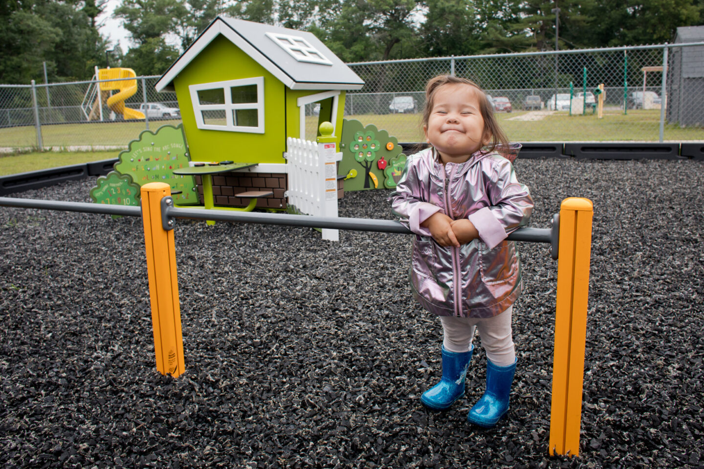 A young child smiles standing on a playground
