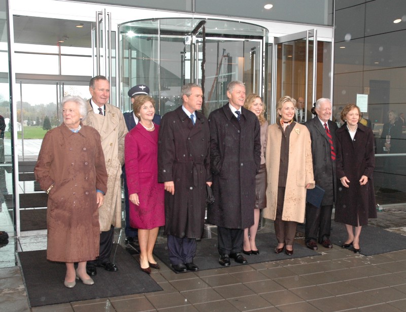 Barbara Bush, President George H. W. Bush, Laura Bush, President George W. Bush, President Bill Clinton, Chelsea Clinton, Secretary Hillary Clinton, President Jimmy Carter, and Rosalynn Carter stand in front of the Clinton Presidential Center