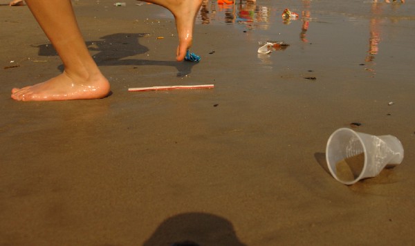 Close-up of person walking on beach with plastic debris