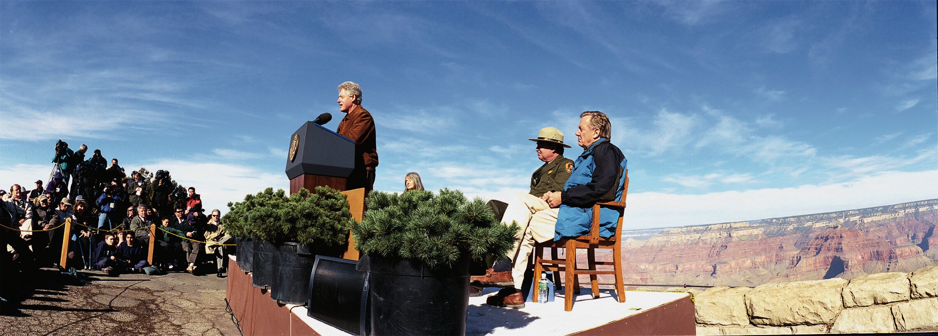 President Clinton speaks to a crowd from behind a podium. Behind him are canyons.
