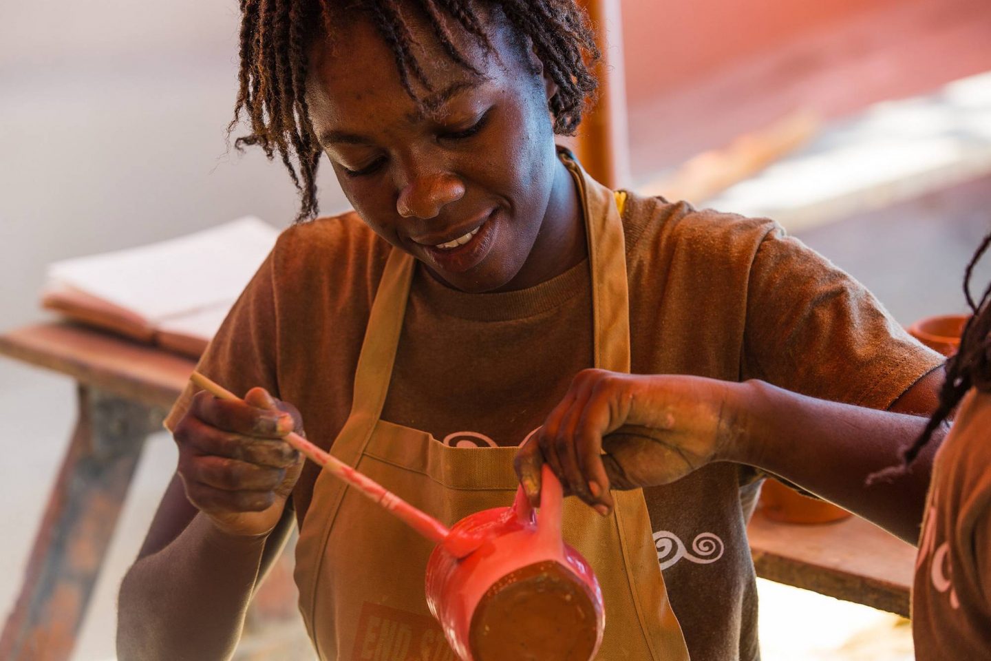 An individual wearing an apron paints a piece of pottery