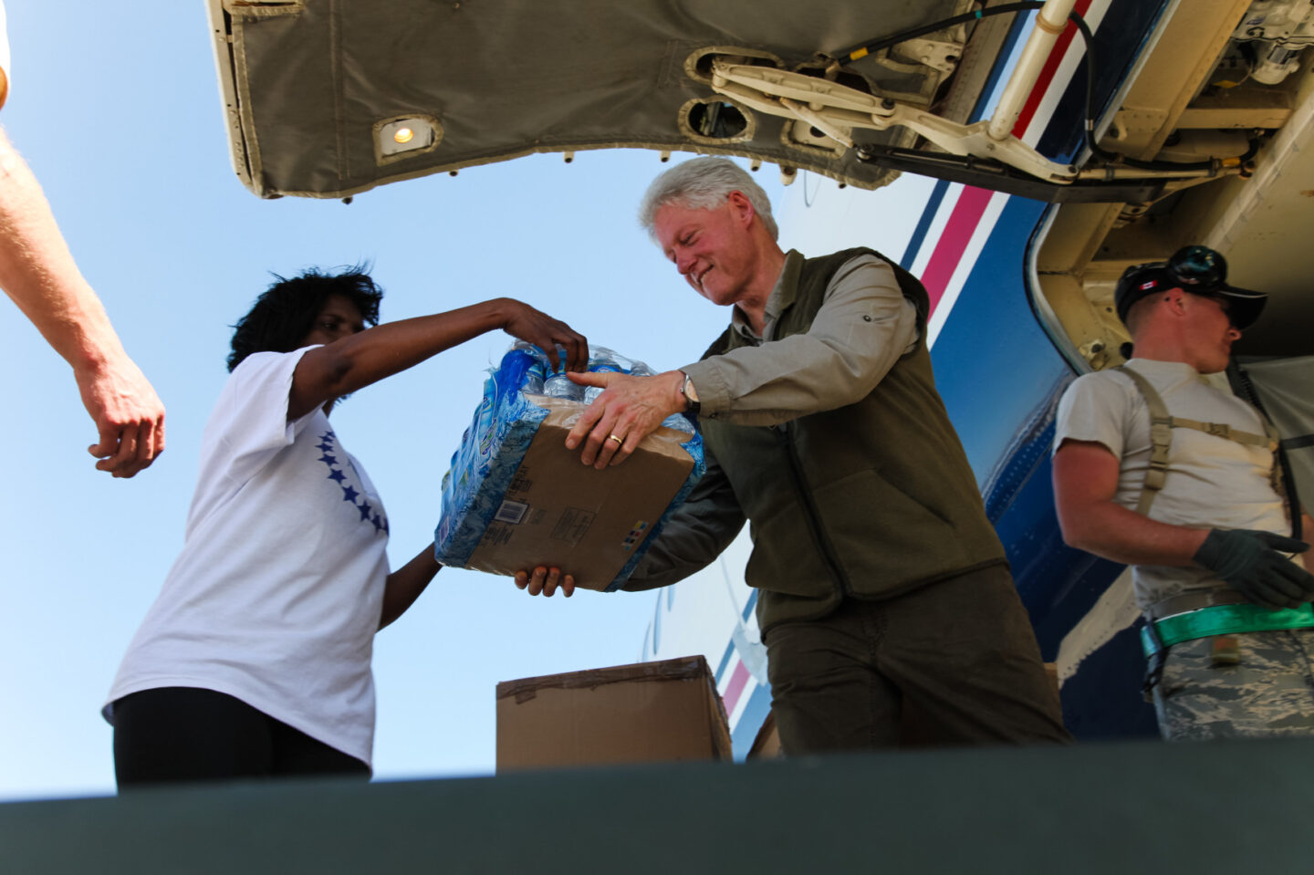 President Clinton and several individuals unload bottles of water from a plane