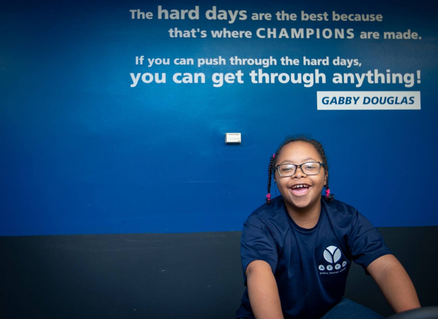A student rides an exercise bike. A wall behind her includes a quote from Gabby Douglas: "If you can push through the hard days, you can get through anything!"