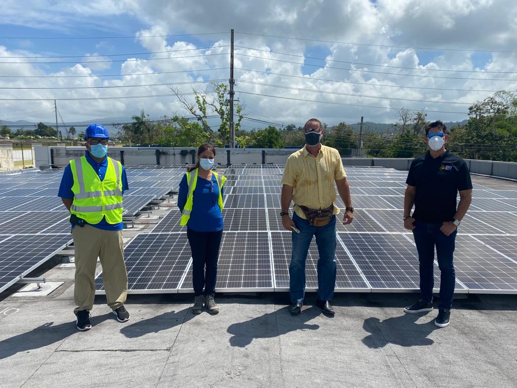 Four individuals stand in front of solar panels