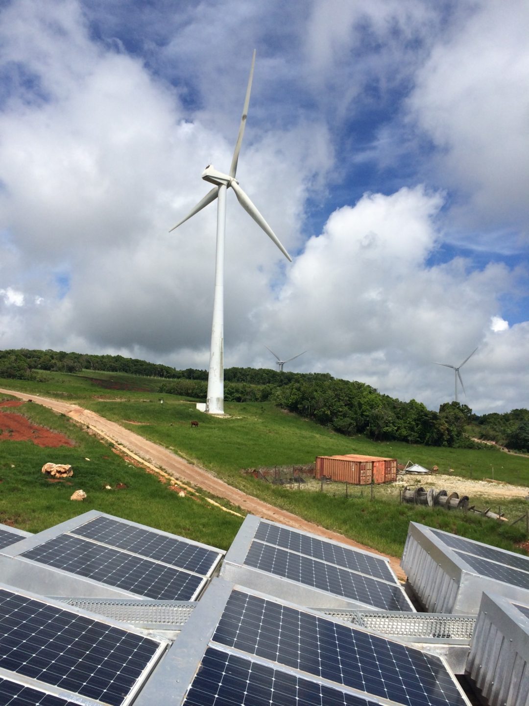 A wind turbine spins behind several solar panels