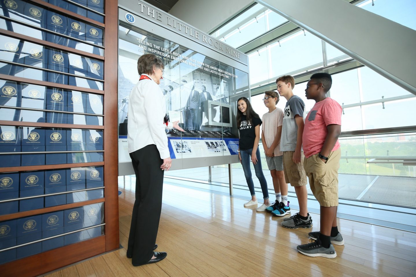 A docent and four students stand near at exhibit about the Little Rock Nine at the Clinton Presidential Center