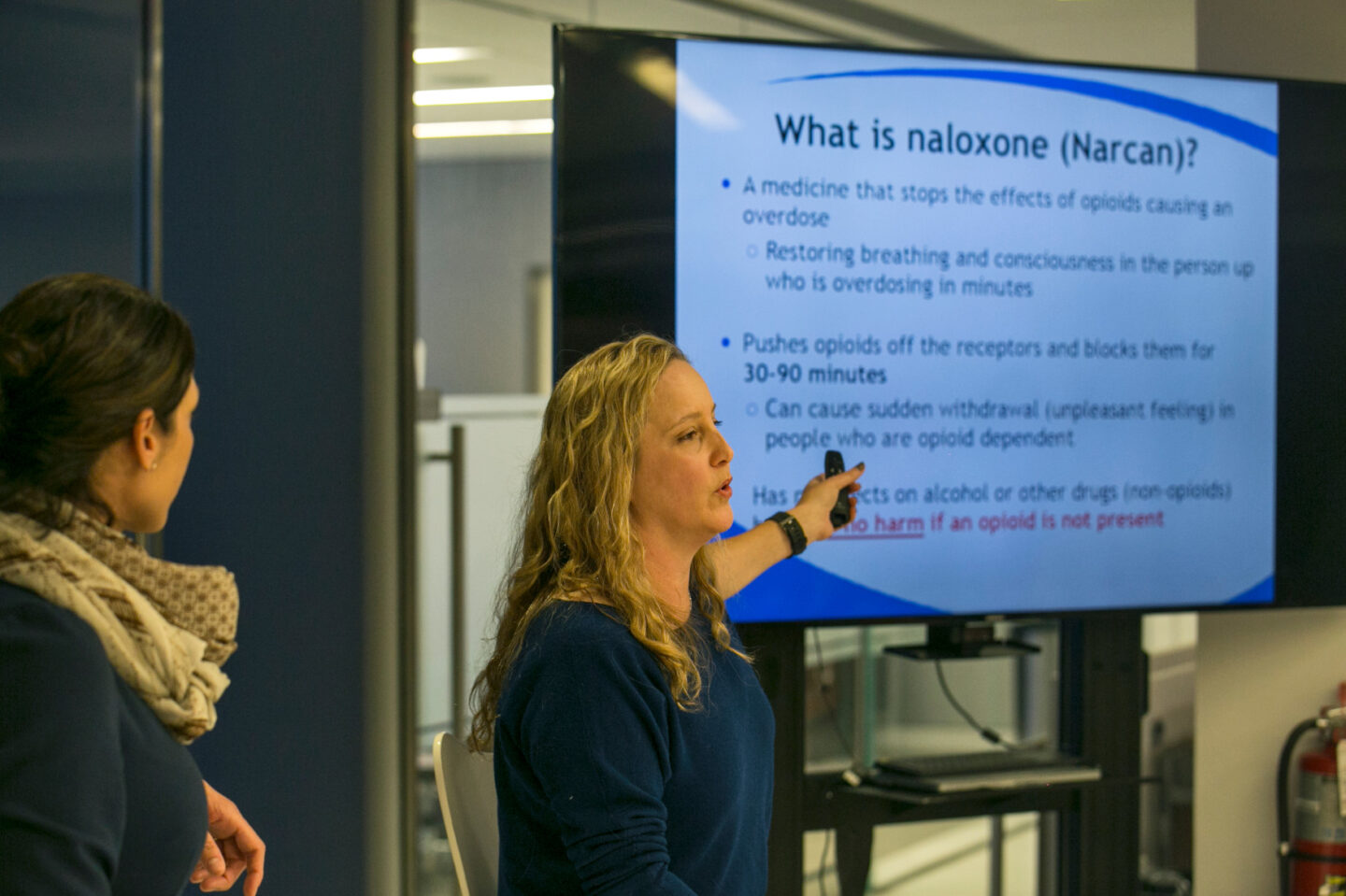 An individual presents in front of a screen that says "What is naloxone (Narcan)?"