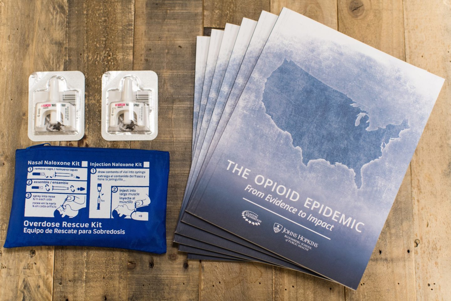 Materials on a table including naloxone nasal spray and a report titled "The Opioid Epidemic: From Evidence To Impact"