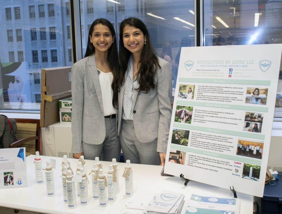 Two individuals stand with samples and information about their project, "Mosquitos Be Gone"