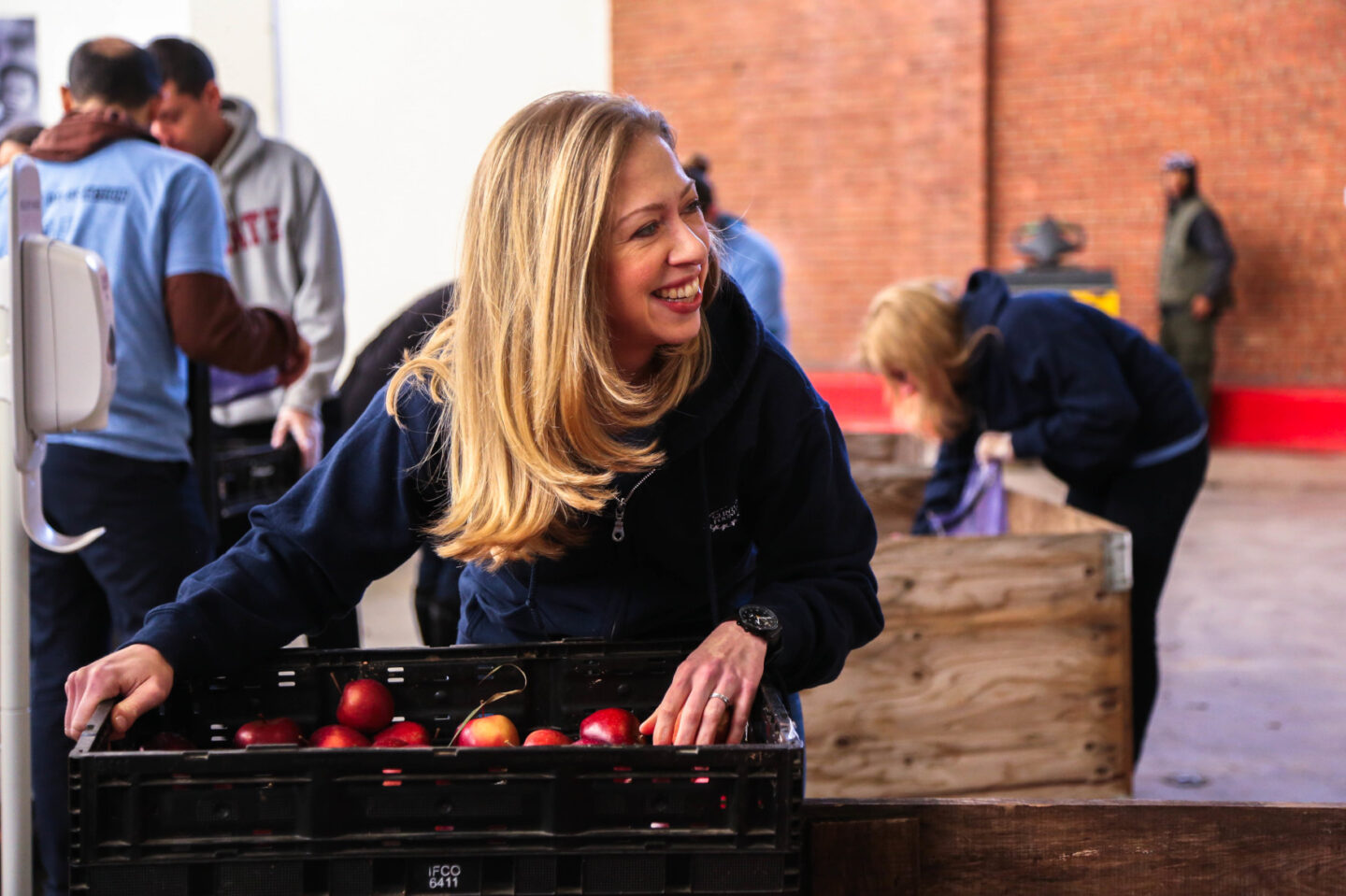 Chelsea Clinton stands over a container of apples