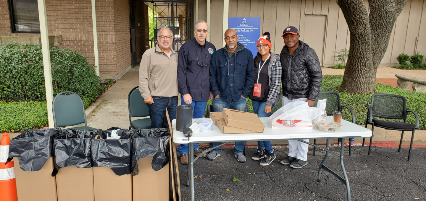 Individuals stand behind a folding table at a Drug Take Back Day event