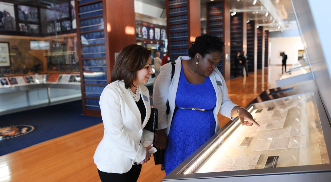 Two individuals examine a document on display at the Clinton Presidential Library