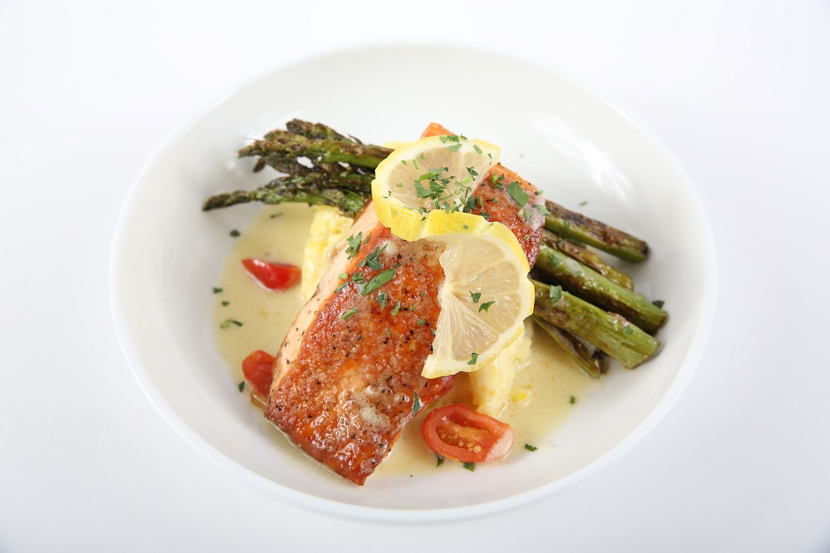 Plated meal which includes fish and asparagus, topped with lemon and herbs