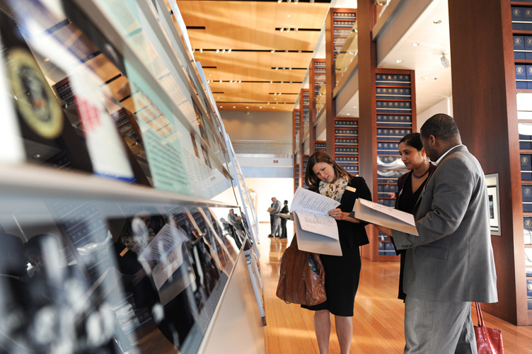Three individuals gather in front of an exhibit at the Clinton Presidential Library