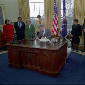 President Clinton signs documents while sitting at the Resolute Desk in the Oval Office