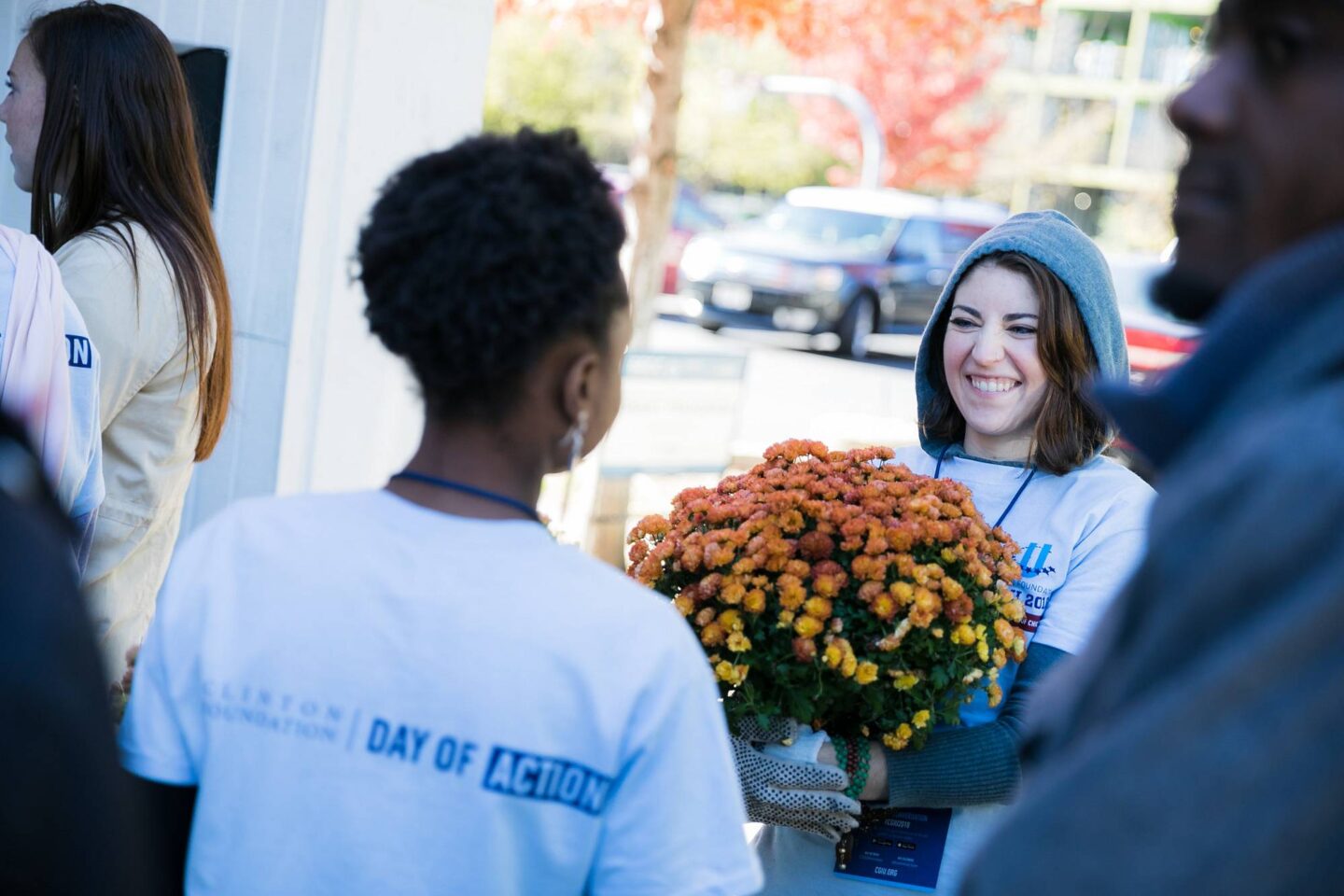 Several individuals stand outside at a volunteer event. They wear blue Day of Action shirts and one is holding orange and yellow flowers.