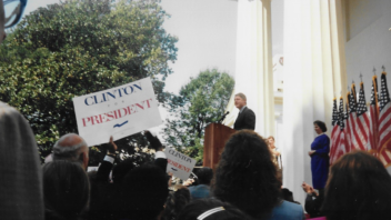 President Clinton stands behind a podium in front of the White House. A crowd is gathered and are holding "Clinton for President" signs.
