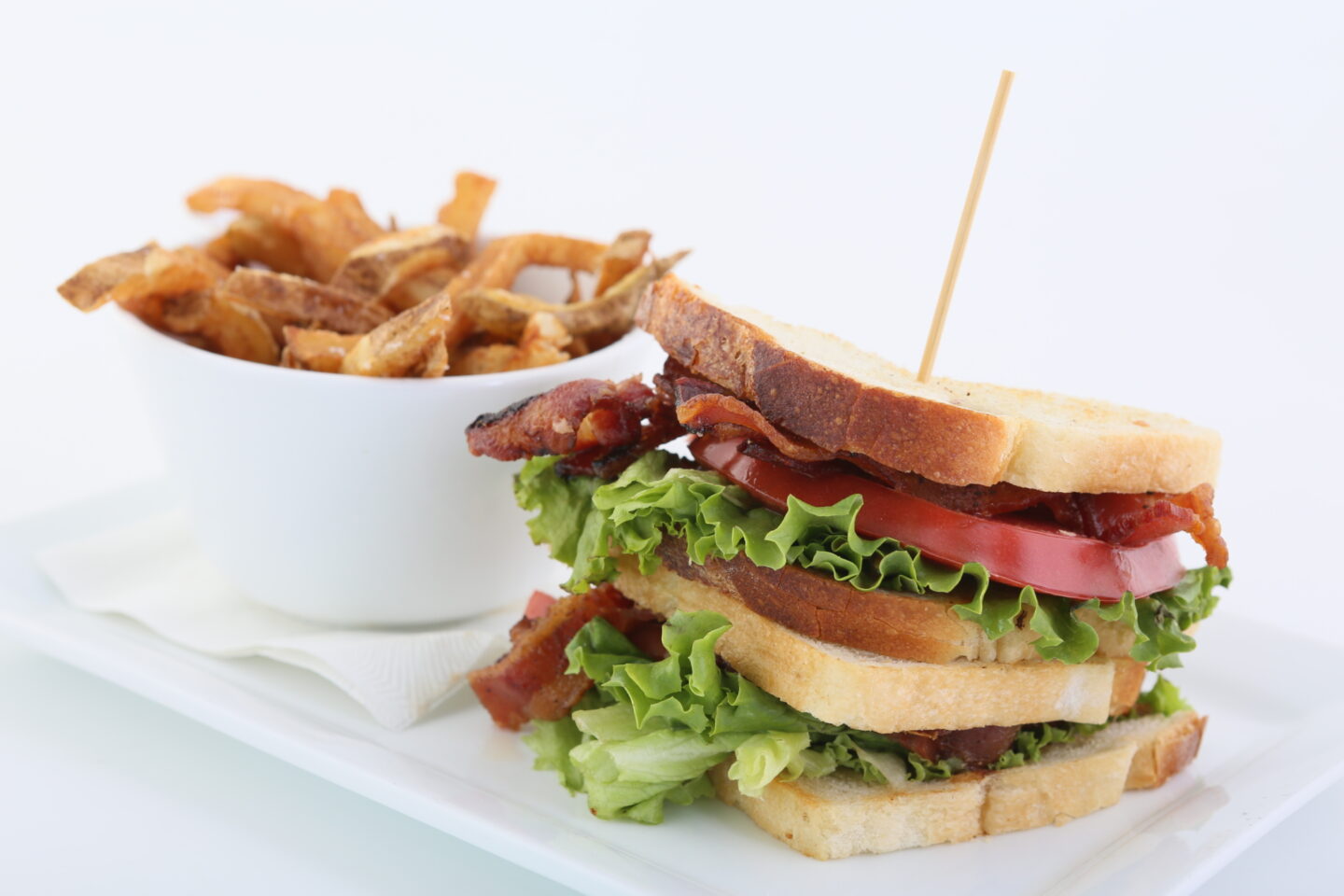 Plated meal which includes a bacon, lettuce, and tomato sandwich along with a side of french fries