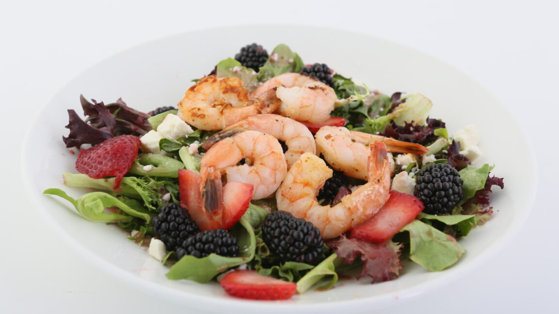 Plated meal which includes a salad with shrimp and berries