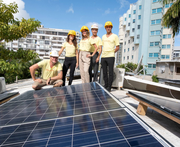 A group of individuals wearing hard hats gather in front of a solar panel