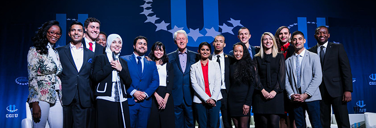President Clinton stands onstage at CGI University with a large group of students