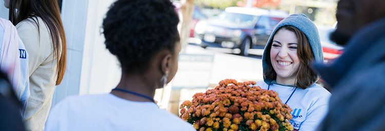 Several individuals stand outside at a volunteer event. They wear blue Day of Action shirts and one is holding orange and yellow flowers.