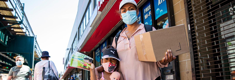 An adult and child stand outside wearing masks and holding books