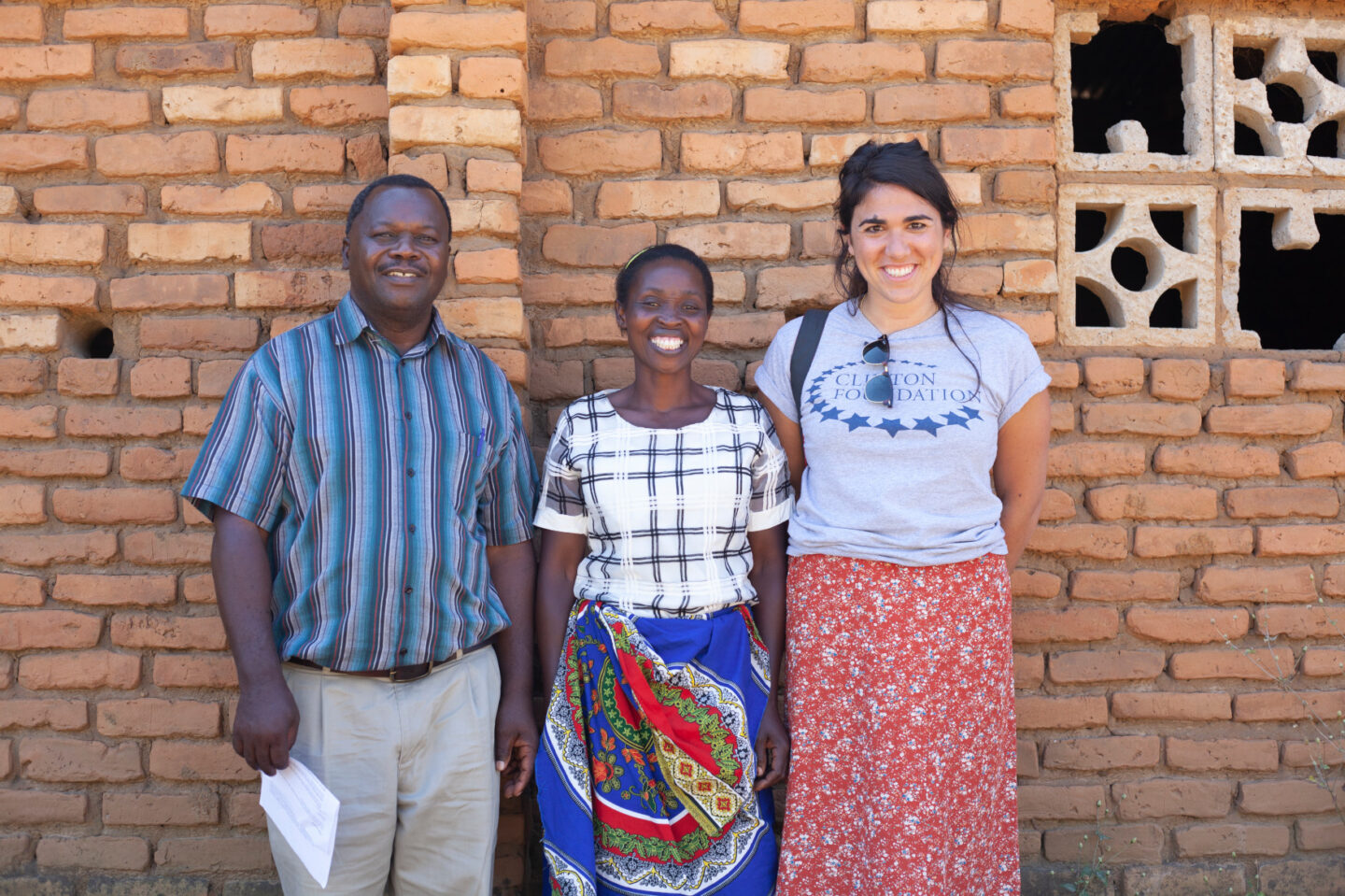 Three individuals stand together in front of a brick building