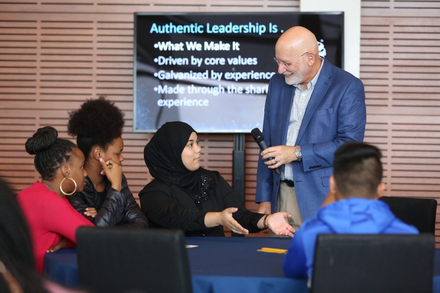 A staff member holds a microphone while speaking with several young people