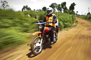 An individual rides a motorcycle on unpaved road