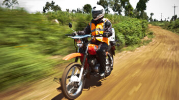 An individual rides a motorcycle on unpaved road