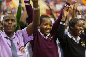 A group of young people in a crowd raise their arms in celebration