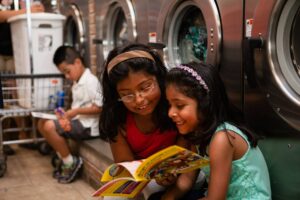 Children read books in front of washing machines in a laundromat