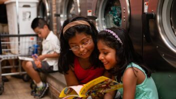 Children read books in front of washing machines in a laundromat