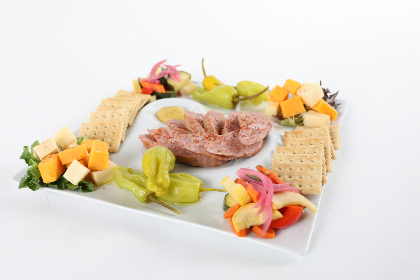 Plated charcuterie board including crackers, deli meat, cheese, and vegetables