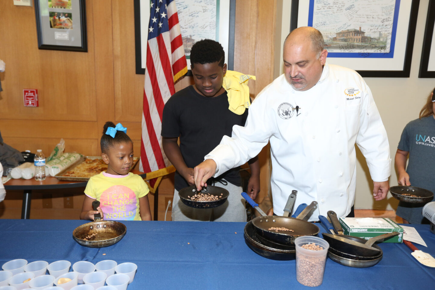 A chef and two students cook using frying pans