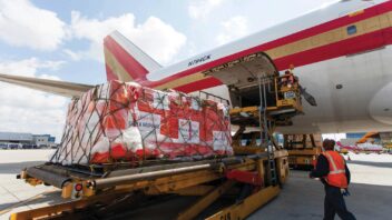 An individual approaches a pallet of medical supplies being loaded onto a plane