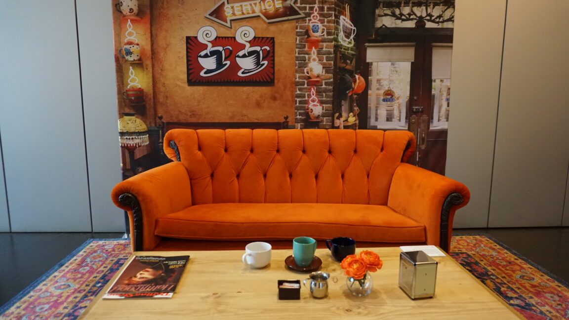 Orange couch displayed in front of backdrop with picture of coffee shop