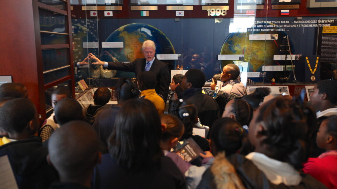 President Clinton stands amid a group of students in front of an exhibit at the Clinton Presidential Center