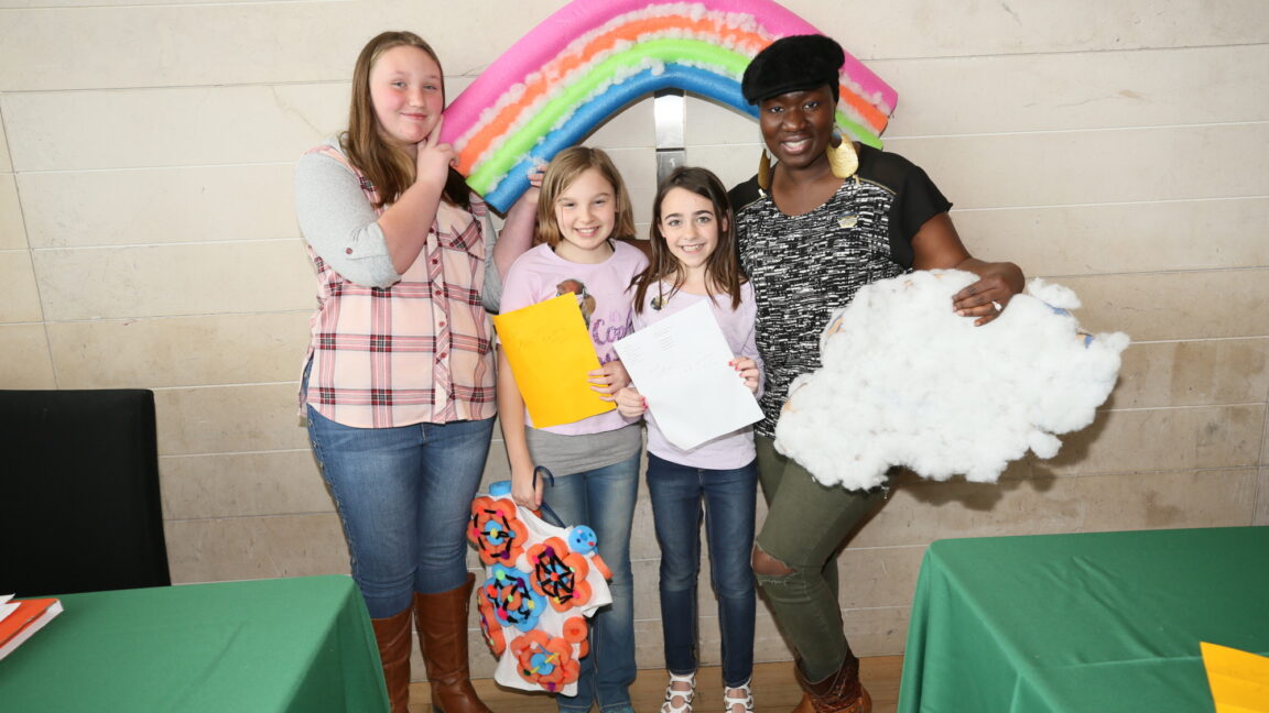 Mentors and mentees pose together with crafts, including a rainbow and cloud