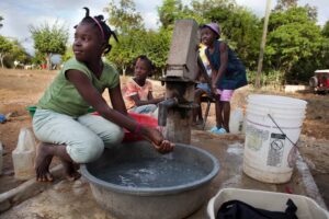 A group of children gather around a water pump