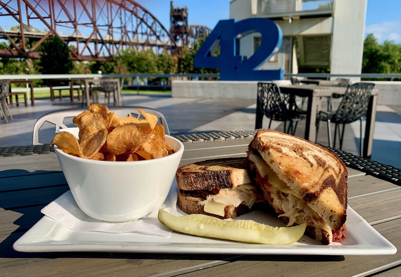Plated meal which includes a reuben sandwich, a side of chips, and a pickle