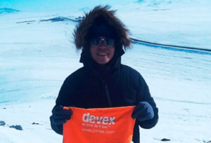 An individual wearing a parka and standing on snow holds a Devex banner