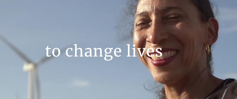 An individual smiles in front of a wind turbine. The words "to change lives" appear.
