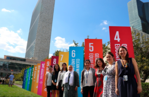 Several individuals stand outside in front of signs that promote the sustainable development goals