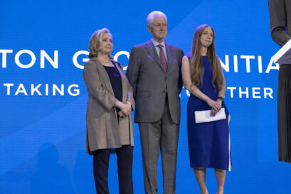 President Clinton, Hillary Clinton, and Chelsea Clinton stand on stage in front of a blue backdrop